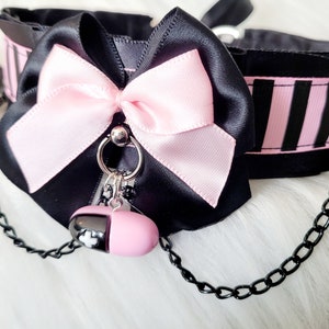 May include: Black choker with a pink satin bow and a pink pill charm attached to a black chain.