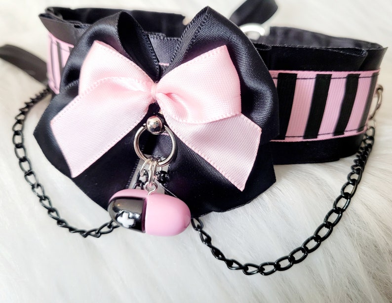 May include: Black choker with a pink satin bow and a pink pill charm attached to a black chain.