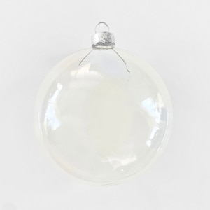May include: A clear, round glass Christmas ornament with a silver metal cap. The ornament is transparent, allowing light to pass through, and has a slight iridescent sheen. The ornament is designed for holiday decoration.