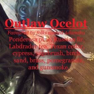 Może przedstawiać: Para czarnych skórzanych kowbojskich butów ze srebrnymi ostrogami. Buty mają ozdobny wzór na skórze, a tekst "Outlaw Ocelot" jest napisany czerwonymi literami. Tekst poniżej brzmi "Favoured by folks named Adamska Ponderosa pine, Russian fir, Labrador tea, Texan cedar, cypress, sagebrush, birch, sand, brass, pomegranate, and gunsmoke."