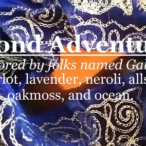 May include: A close-up of a blue fabric with white embroidery. The text "Blond Adventurer" is written in white letters. The text "Favored by folks named Gabrielle Merlot, lavender, neroli, allspice, oakmoss, and ocean." is written in white letters.