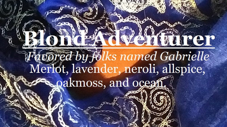 May include: A close-up of a blue fabric with white embroidery. The text "Blond Adventurer" is written in white letters. The text "Favored by folks named Gabrielle Merlot, lavender, neroli, allspice, oakmoss, and ocean." is written in white letters.
