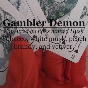 May include: A red leather glove with playing cards on top. The cards are face up and show the 8 of hearts and the 8 of spades. The text on the cards reads "Gambler Demon Favoured by folks named Husk Tobacco, white musk, peach brandy, and vetiver."