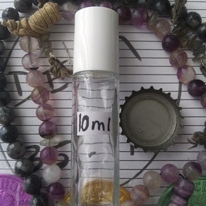 May include: A clear glass bottle with a white cap and a label that says "10 ml". The bottle is surrounded by purple and gray beads.