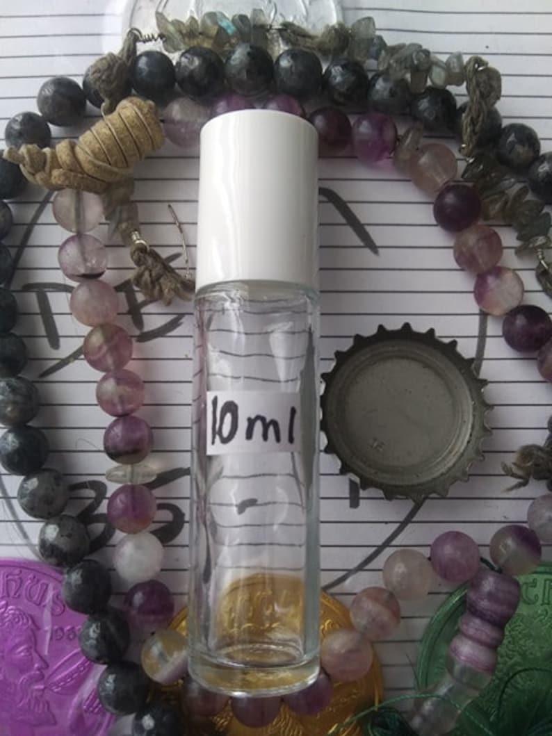 May include: A clear glass bottle with a white cap and a label that says "10 ml". The bottle is surrounded by purple and gray beads.