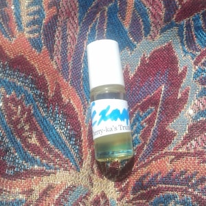 Puede incluir: Una pequeña botella de vidrio transparente con una tapa blanca y una etiqueta azul y blanca que dice "Cherry-ka's Trunk".