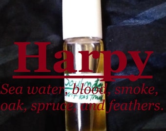 May include: A clear glass bottle with a white cap and a label that reads "Soulmate" and "Harpy". The label also lists the scent notes: "Sea water, blood, smoke, oak, spruce, and feathers."