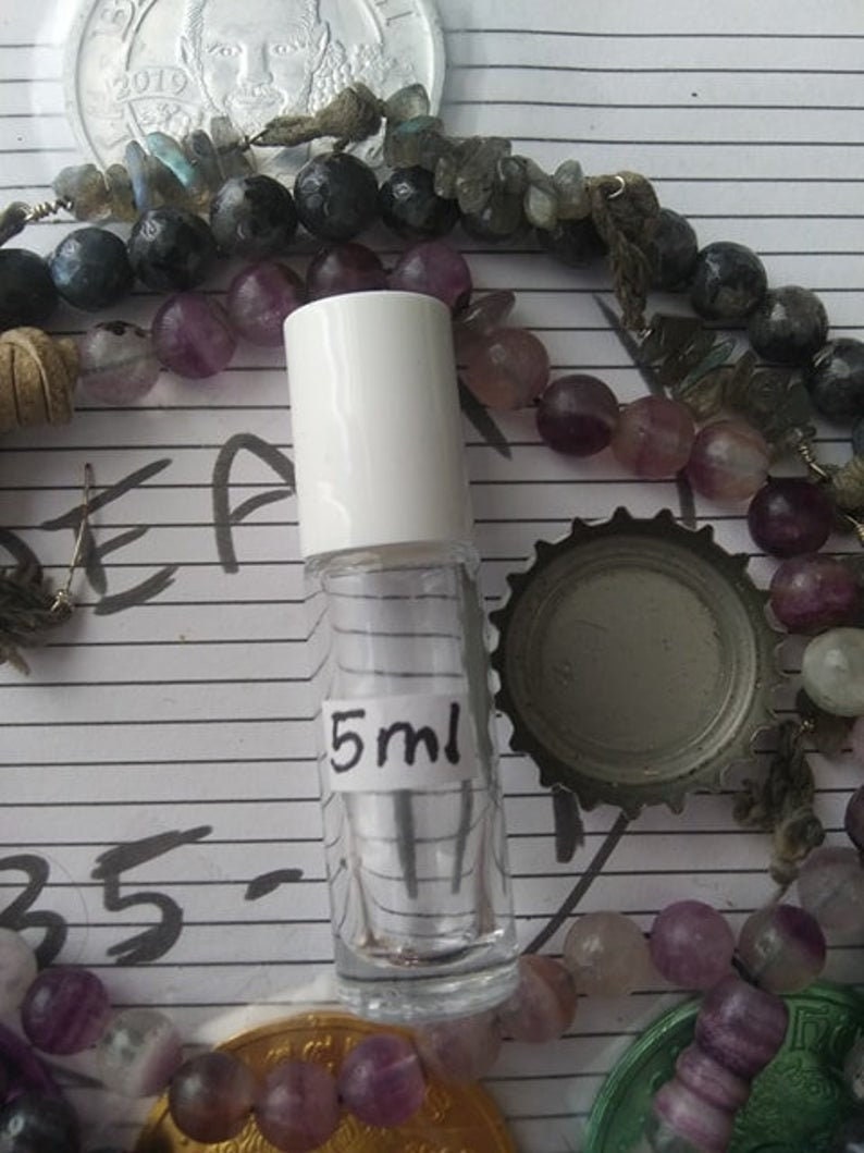 May include: A clear glass bottle with a white cap and a label that says "5 ml". The bottle is sitting on a surface with a variety of colorful beads.