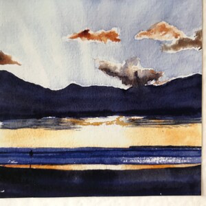 A watercolor painting of a seascape with a blue sky, brown clouds, and a dark blue mountain range in the background. The foreground shows a blue ocean with a yellow sandy beach.