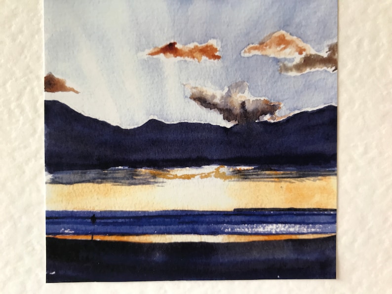 A watercolor painting of a seascape with a blue sky, brown clouds, and a dark blue mountain range in the background. The foreground shows a blue ocean with a yellow sandy beach.