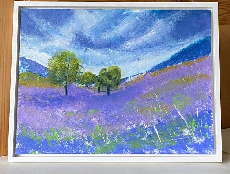 An acrylic painting of a landscape scene. The foreground is a field of purple flowers with green accents. In the mid-ground are green trees and a rolling hill. The background features a blue sky with white clouds and blue mountains.