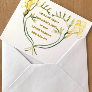 A white envelope containing a greeting card. The card displays yellow floral illustrations and gold text reading "John and Susan CONGRATULATIONS on your GOLDEN WEDDING ANNIVERSARY!". The card is partially visible.