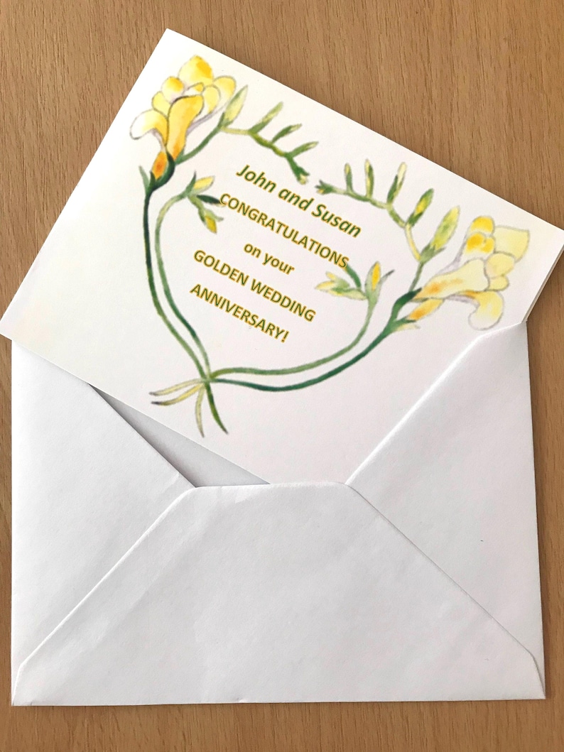 A white envelope containing a greeting card. The card displays yellow floral illustrations and gold text reading "John and Susan CONGRATULATIONS on your GOLDEN WEDDING ANNIVERSARY!". The card is partially visible.