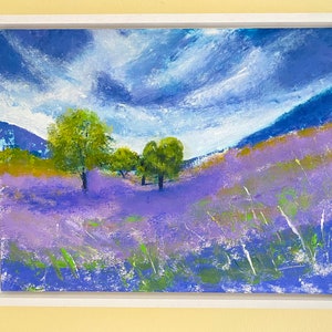 May include: An original landscape painting in a white frame. The artwork depicts a field of lavender flowers under a cloudy blue sky. Green trees and grass add contrast to the purple and blue hues. The painting evokes a sense of tranquility.