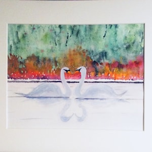 May include: Watercolor painting of two white swans with orange beaks, facing each other on a body of water. The swans' reflections create a heart shape. The background features a colorful mix of green, orange, and red foliage.