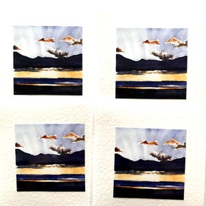 Four blank greeting cards with watercolor paintings of a sunset over a mountain range and a body of water. The cards are white with a textured surface. The paintings are in shades of blue, purple, brown, and yellow.