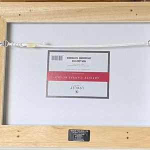 May include: Back of a framed canvas board, with a light wood frame. The canvas is labeled "ARTISTS' CANVAS BOARD" and measures 12 x 16 inches. A white cord is strung across the back for hanging.