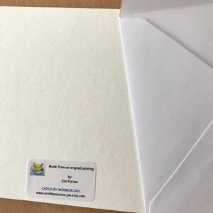 A white card with a sticker on the bottom right corner. The sticker is white with a blue and yellow banana illustration in the top left corner. The sticker says 'Made from an original painting by Jan Purves CARDS BY MORMORJAN www.cardsbymormorjan.etsy.com'.