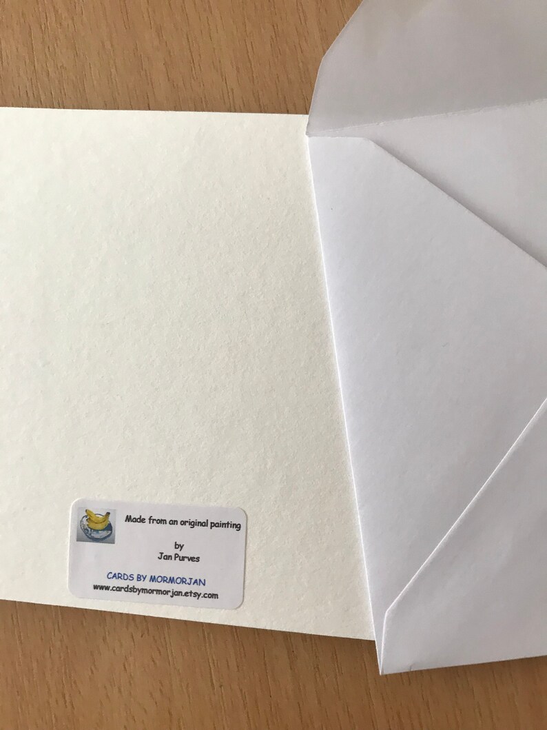 A white card with a sticker on the bottom right corner. The sticker is white with a blue and yellow banana illustration in the top left corner. The sticker says 'Made from an original painting by Jan Purves CARDS BY MORMORJAN www.cardsbymormorjan.etsy.com'.
