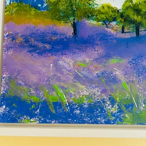 May include: An original acrylic painting of a lavender field with trees under a blue sky. The artwork is framed in a white wooden frame. The painting features shades of purple, blue, green, and white, creating a vibrant landscape scene.