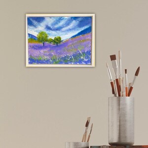 May include: Framed landscape painting depicting a field of purple flowers under a blue sky with white clouds. Green trees are in the middle ground. The painting is in a white frame.