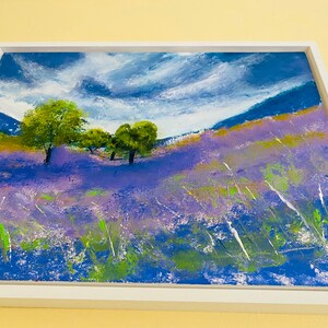 May include: An original landscape painting in a white frame. The artwork depicts a field of purple flowers under a blue sky with white clouds. Green trees and grass are also visible, creating a serene and colorful scene.