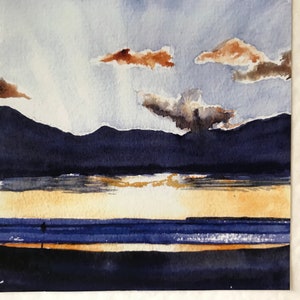 K&ouml;nnte beinhalten: Aquarellmalerei eines Sonnenuntergangs &uuml;ber dem Wasser. Der Himmel ist eine Mischung aus Blau und Wei&szlig; mit braunen Wolken. Dunkelblaue Berge befinden sich im Hintergrund. Eine Person steht am Strand.