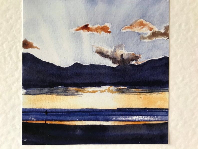 K&ouml;nnte beinhalten: Aquarellmalerei eines Sonnenuntergangs &uuml;ber dem Wasser. Der Himmel ist eine Mischung aus Blau und Wei&szlig; mit braunen Wolken. Dunkelblaue Berge befinden sich im Hintergrund. Eine Person steht am Strand.