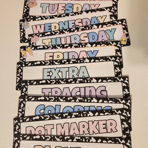May include: A collection of rectangular cards featuring the days of the week and activity names. Each card has a white background with a black and white patterned border. The cards display the words "MONDAY", "TUESDAY", "WEDNESDAY", "THURSDAY", "FRIDAY", "EXTRA", "TRACING", "COLORING", "DOT MARKER", and "PLAYDOH".