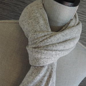 May include: A gray and white speckled scarf is draped around a mannequin's neck. The scarf is soft and cozy, perfect for keeping warm in the winter.