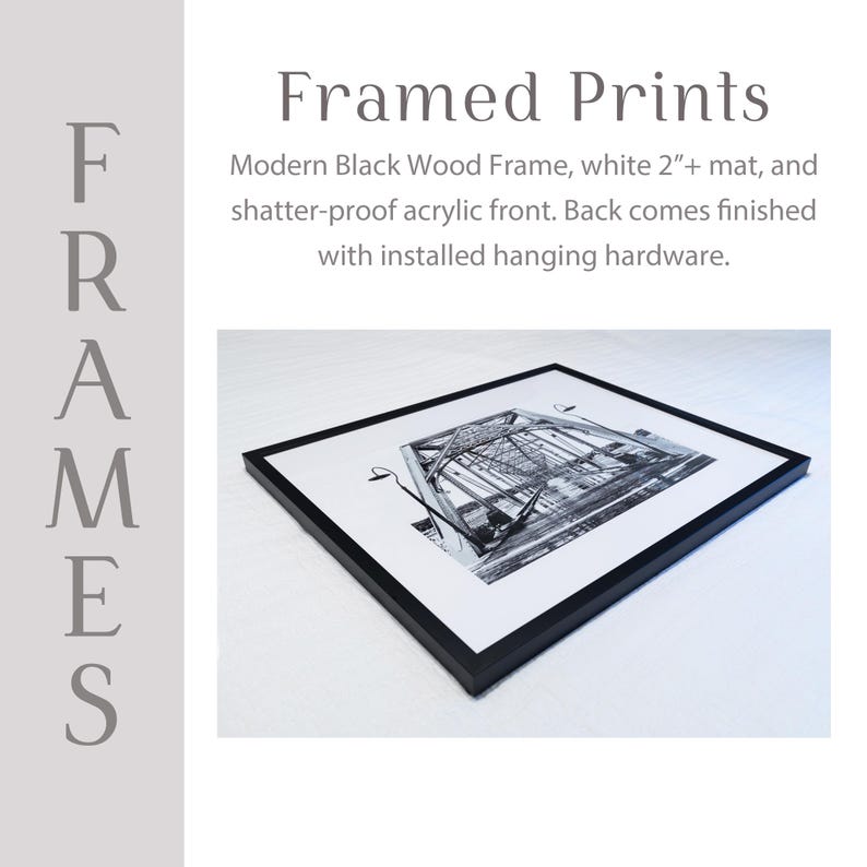 The image is a framed print featuring a black and white photograph of a bridge. The print is placed on a white surface and has a modern black wood frame. The back of the print includes a white mat and a shatter-proof acrylic front. The print is finished with installed hanging hardware.
