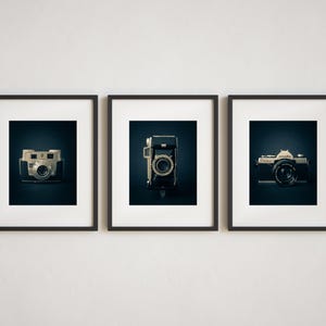 May include: Three framed photographs featuring vintage cameras. The cameras are in black and silver, with a dark background. The frames are dark brown, and the overall aesthetic is classic and nostalgic.