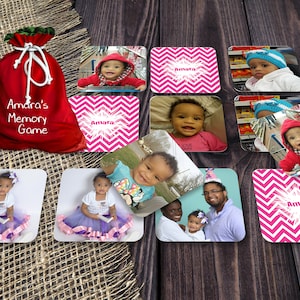 May include: A red fabric bag with the text "Amara's Memory Game" printed on it. The bag is surrounded by 10 square cards with photos of a baby girl and a pink and white chevron pattern with the name "Amara" printed on them.