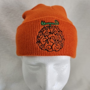 May include: Orange knitted beanie with a black and green embroidered design of a skull with flames.