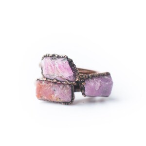 May include: A ring with three pink and white raw gemstones set in copper wire.