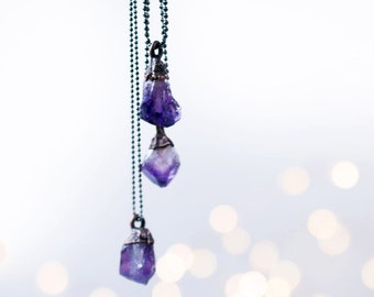May include: A silver chain necklace with three amethyst crystal pendants. The crystals are different shapes and sizes, and the chain is delicate.