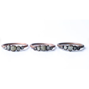 May include: Three copper rings with a row of small, rough, grey diamonds set in each band.