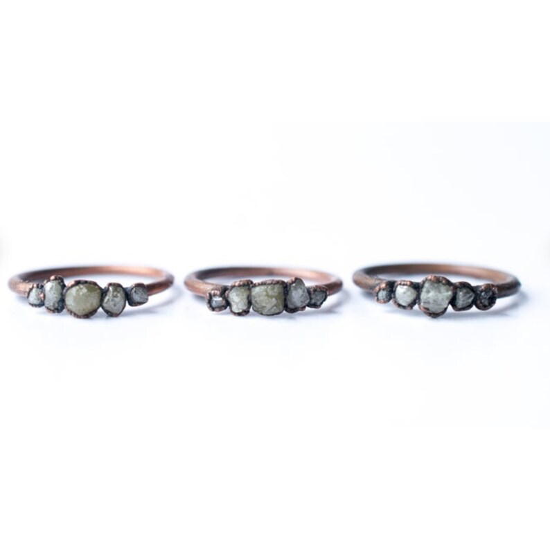 May include: Three copper rings with a row of small, rough, grey diamonds set in each band.