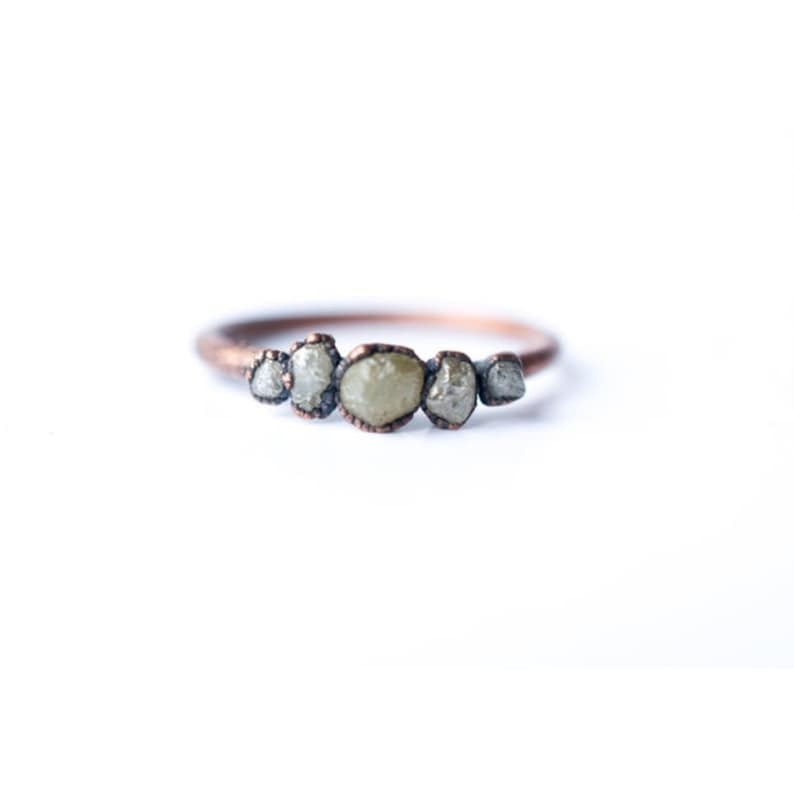 May include: A copper ring with five rough, grey diamonds set in a row.