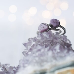 May include: Two rings with purple gemstone settings on a bed of amethyst crystals.