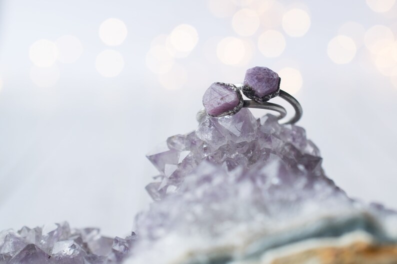 May include: Two rings with purple gemstone settings on a bed of amethyst crystals.