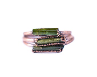 May include: A copper ring with three green tourmaline stones wrapped around the band.