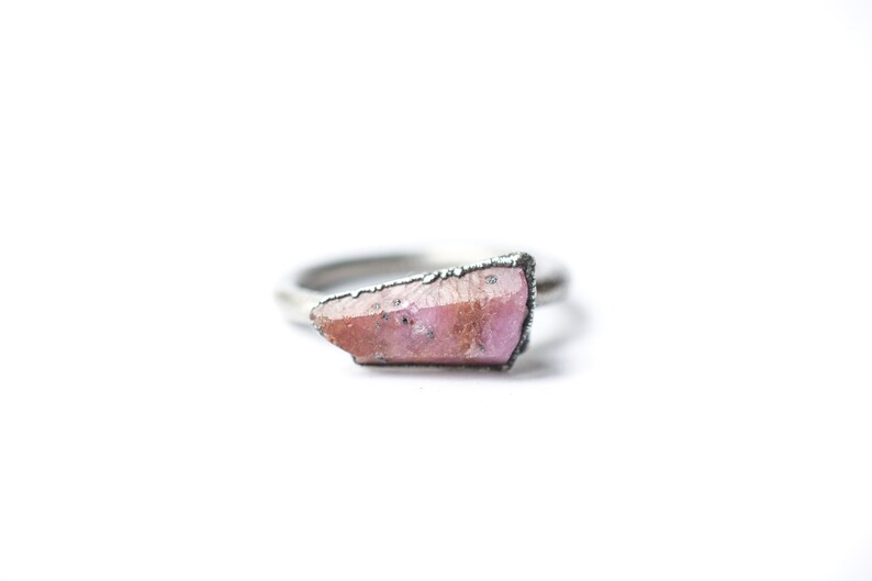 Puede incluir: Un anillo de plata con una piedra preciosa rosa en bruto de forma irregular engastada en la banda.
