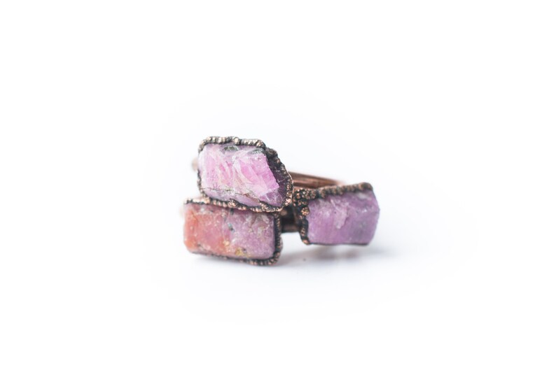 May include: A ring with three pink and white raw gemstones set in copper wire.