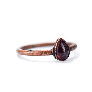 May include: A copper ring with a teardrop-shaped garnet gemstone.