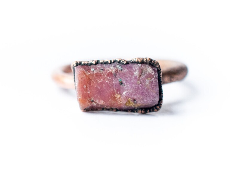 May include: A copper ring with a raw pink gemstone set in the center.