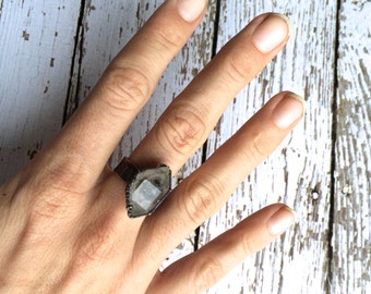 Può includere: Un anello d'argento con una pietra preziosa trasparente sfaccettata incastonata in una forma geometrica.