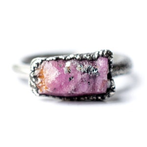 Puede incluir: Un anillo de plata con una piedra preciosa en bruto de color rosa y naranja engastada en la banda.