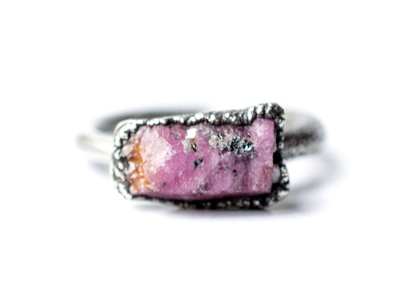 Puede incluir: Un anillo de plata con una piedra preciosa en bruto de color rosa y naranja engastada en la banda.
