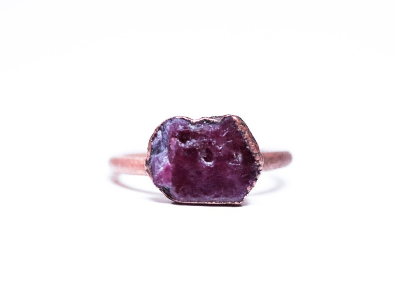 May include: A copper ring with a raw, purple ruby gemstone set in the centre.